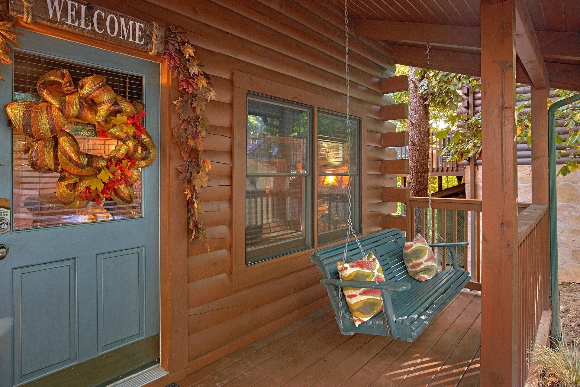 Een houten chalet met een 'WELCOME' bord, een veranda met een schommel, en een raam met herfstbladeren.