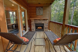 A wooden deck with a stone fireplace, two wicker chairs, and a glass door leading to an indoor seating area. - Pool N Around | Indoor Pool, Hot Tub, Near Dollywood, Game Room, Fireplace + Free Attraction Tickets (Pigeon Forge)