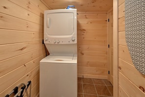 A compact laundry room with a stacked washer and dryer, wooden walls, and a tiled floor. - Pool N Around | Indoor Pool, Hot Tub, Near Dollywood, Game Room, Fireplace + Free Attraction Tickets (Pigeon Forge)