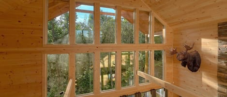 Un interior de madera con ventanas amplias, una escalera y una cabeza de animal montada.