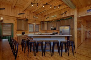 A wooden interior with a kitchen island, bar stools, and a refrigerator. - Poolside Lodge Cabin Rental (Sevierville)