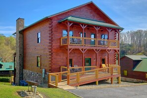 A log cabin with a balcony and a stone chimney. - Poolside Lodge Cabin Rental (Sevierville)