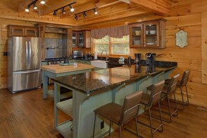 A kitchen with a stainless steel refrigerator, a stove, a sink, and a large island with bar stools. - Grand Mountain Lodge | Sleeps 26, Theater, Mtn Views, Hot Tub, Game Room + Free Attraction Tickets (Pigeon Forge)