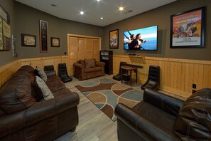 A living room with a television, leather sofas, a wooden panel wall, and framed movie posters. - Grand Mountain Lodge | Sleeps 26, Theater, Mtn Views, Hot Tub, Game Room + Free Attraction Tickets (Pigeon Forge)