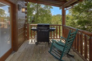 A wooden deck with a grill and a chair. - Grand Mountain Lodge | Sleeps 26, Theater, Mtn Views, Hot Tub, Game Room + Free Attraction Tickets (Pigeon Forge)
