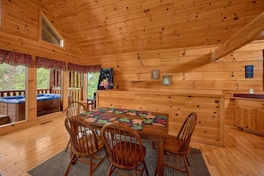 Ein Holzblockhaus-Interieur mit Esstisch, Stühlen, einer Whirlwanne und einem Kamin.