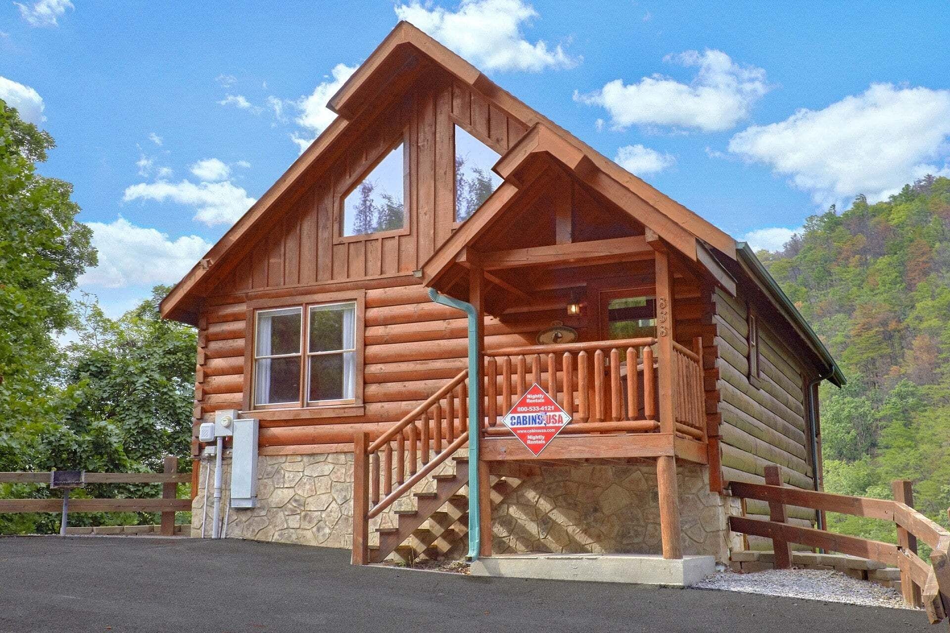 A wooden cabin with a stone foundation, a porch with a wooden railing, and a sign indicating it is a rental property.