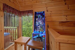 Eine Holzhütte mit einem Holztisch und einem vertikalen Arcade-Spielgerät.