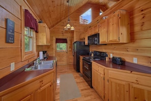 Ein Holzblockhaus-Interieur mit einer Küche, die einen Kühlschrank, einen Herd, eine Mikrowelle und ein Waschbecken umfasst.