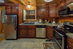 A kitchen with wooden cabinets, stainless steel appliances, a dishwasher, a coffee maker, and a stove. - Restin Easy | Hot Tub, Game Room, Fire Pit, Fireplace + Free Attraction Tickets (Sevierville)