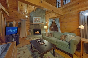 A cozy cabin interior with a stone fireplace, a television, and a comfortable seating area. - Restin Easy | Hot Tub, Game Room, Fire Pit, Fireplace + Free Attraction Tickets (Sevierville)
