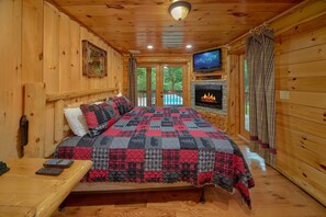 Ein Schlafzimmer einer Holzhütte mit Bett, Fernseher, Kamin und Blick ins Freie.