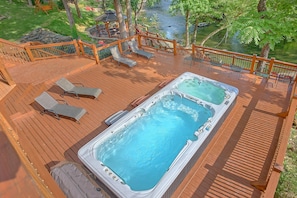 Ein Whirlpool auf einer Holzterrasse mit Liegestühlen, mit Blick auf einen Teich.
