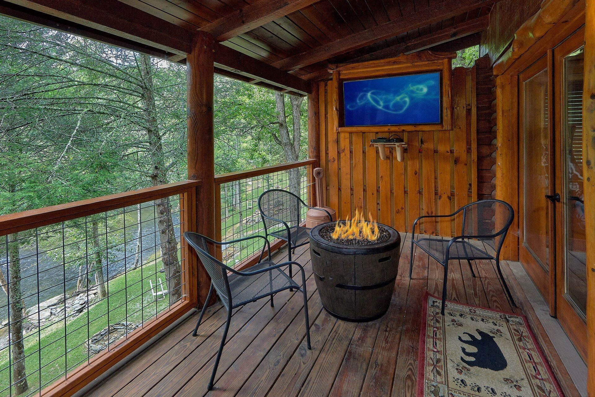 A wooden deck with a fire pit and chairs, overlooking a river.
