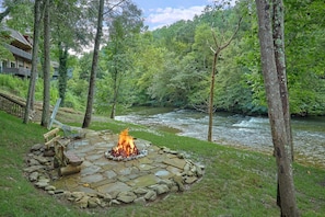 A stone fire pit surrounded by a river and forest. - River Edge | Hot Tub, Game Room, Sleeps 10, Fire Pit, Pet Friendly + Free Attraction Tickets (Sevierville)