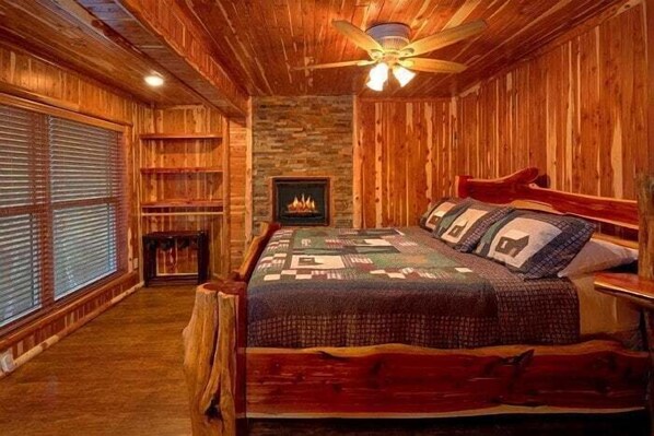Ein Holzblockhaus-Interieur mit Bett, Kamin und Deckenventilator.