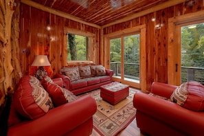 Ein Interieur einer Blockhütte mit einem roten Ledersofa, passendem Hocker und einem großen Fenster mit Blick auf den Wald.