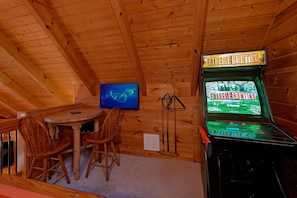 Ein Holzblockhaus-Interieur mit Billardtisch, Stühlen, Fernseher und einer Spielautomaten namens 'EXTREME HUNTING'.