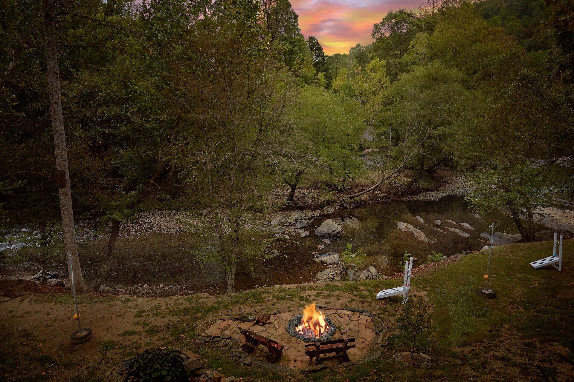A campsite with a fire pit surrounded by rocks, a small stream, and dense forest.
