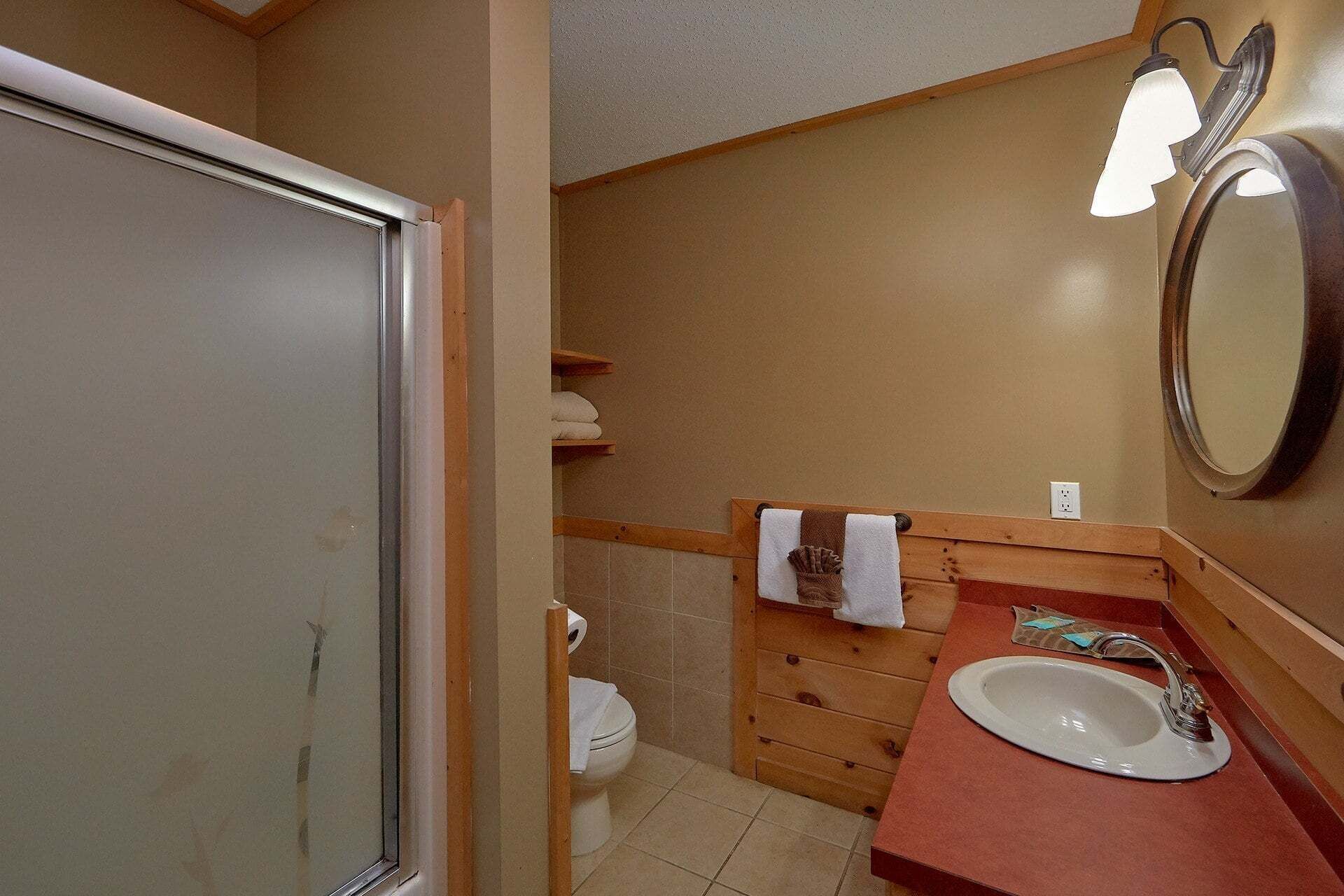A bathroom with a shower, toilet, wooden vanity, sink, and a mirror.