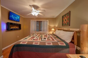 Ein Schlafzimmer mit einem Bett, einem Deckenventilator, einem Fernseher, einem Kamin und einem Fenster mit Jalousien.