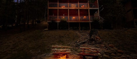 Une cabane en bois à deux étages, avec un foyer au premier plan.