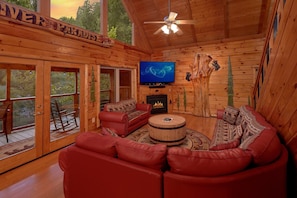 Ein Interieur einer Holzhütte mit einem roten Ledersofa, einem Fernseher, einem Kamin und einem Deckenventilator.