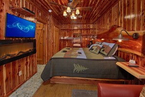 A wooden cabin interior with a bed, a television, and a ceiling fan. - River Pleasures | Hot Tub, Game Room, Sleeps 10, Fire Pit, Pet Friendly + Free Attraction Tickets (Sevierville)