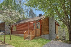 A log cabin with a wooden staircase leading to a porch, surrounded by trees and a clear sky. - River Pleasures | Hot Tub, Game Room, Sleeps 10, Fire Pit, Pet Friendly + Free Attraction Tickets (Sevierville)