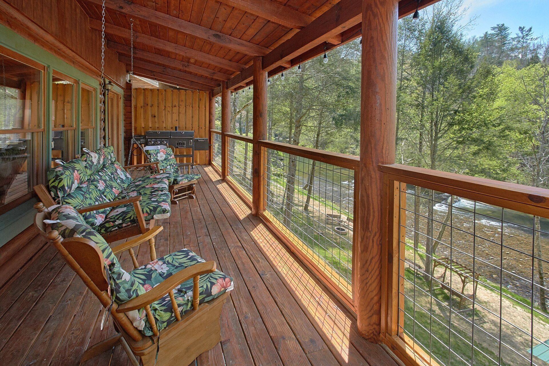 A covered outdoor deck with wooden flooring, a grill, and a seating area with floral-patterned cushions.