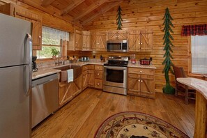 A wooden cabin kitchen with a refrigerator, microwave, stove, and sink. - River Pleasures | Hot Tub, Game Room, Sleeps 10, Fire Pit, Pet Friendly + Free Attraction Tickets (Sevierville)