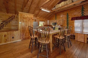 A rustic wooden cabin interior with a dining area featuring a wooden table and chairs, a kitchen with modern appliances, and a cozy ambiance. - River Pleasures | Hot Tub, Game Room, Sleeps 10, Fire Pit, Pet Friendly + Free Attraction Tickets (Sevierville)