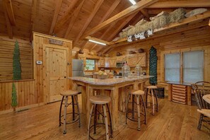 Ein rustikales Holzinterieur mit Küchenbereich, Holzbarhocker und einem großen Fenster.