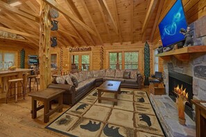 A log cabin interior with a large sectional sofa, a fireplace, a television, and a dining area. - River Retreat | Hot Tub, Game Room, Sleeps 10, Pet Friendly, Fireplace + Free Attraction Tickets (Sevierville)