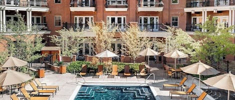 A poolside area with lounge chairs and umbrellas, surrounded by brick buildings with balconies.
