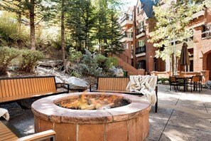 Un foyer entouré de bancs et un espace repas aménagé avec du mobilier d’extérieur.
