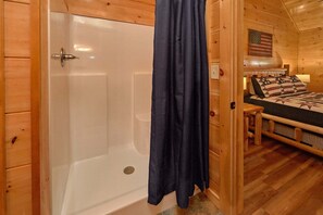 Interior de una cabaña de madera con una bañera, una cama con ropa de cama estampada y una bandera estadounidense en la pared.