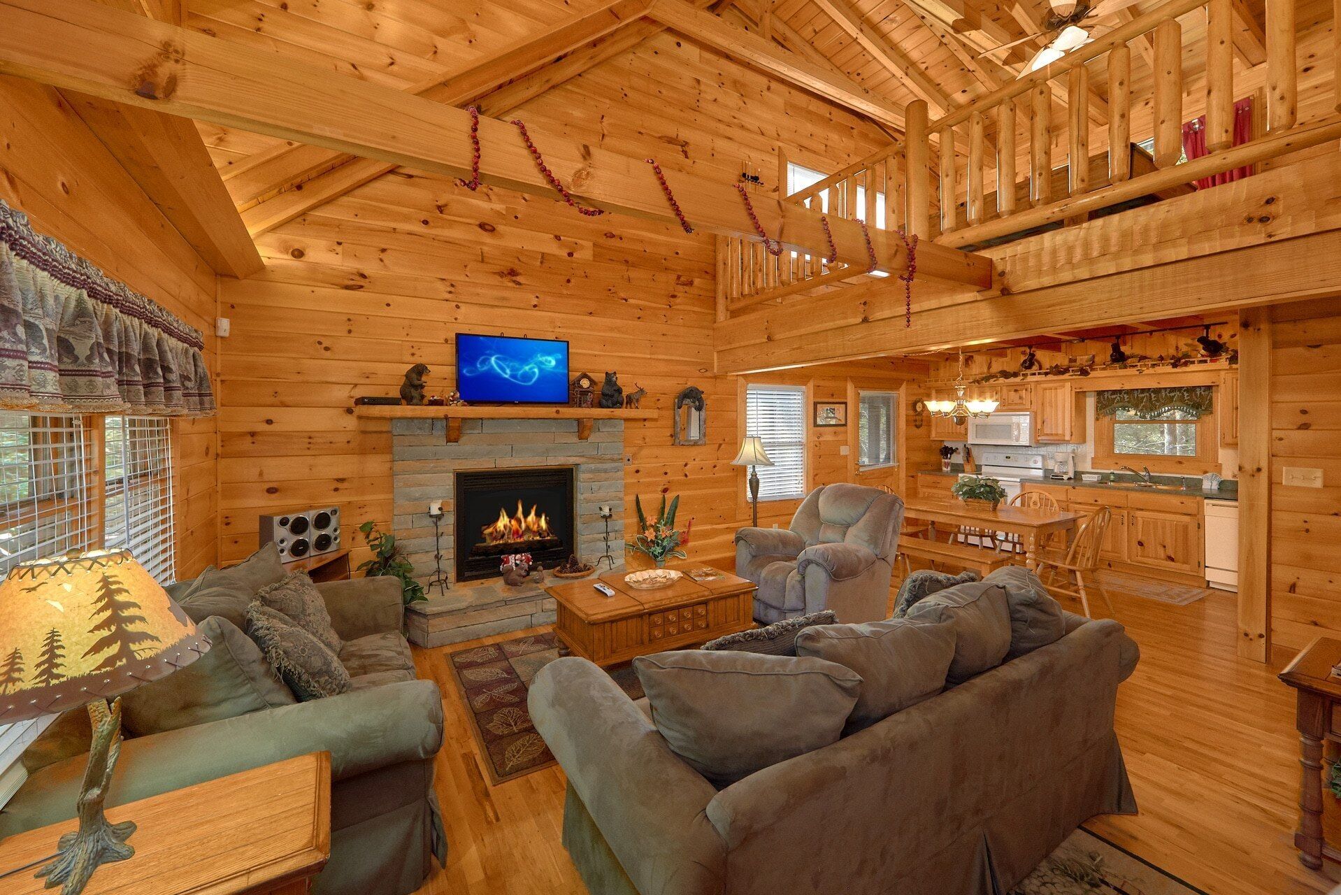A cozy log cabin interior with a fireplace, comfortable seating, a television, and a kitchen area.