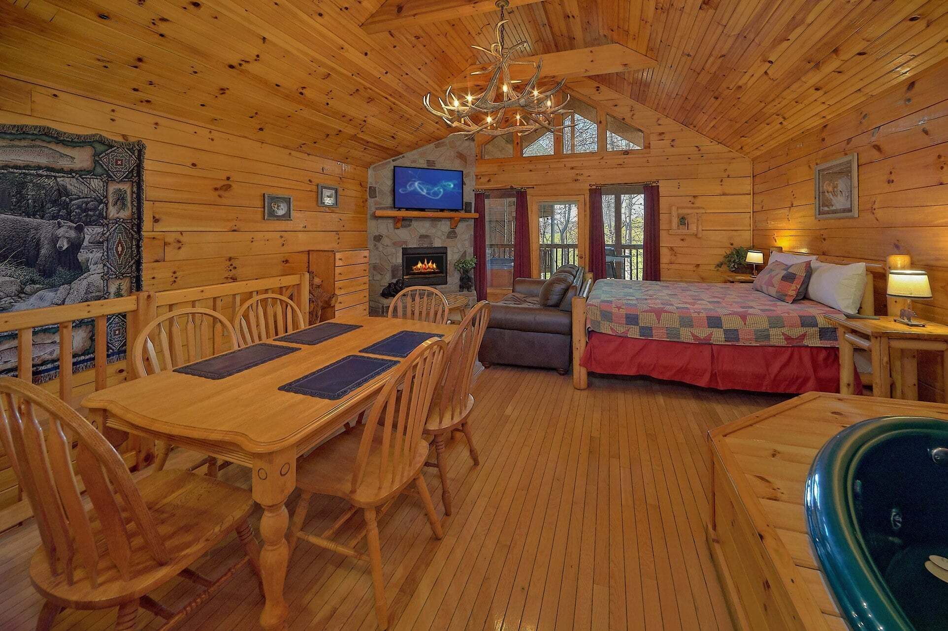A wooden cabin interior with a dining area, a fireplace, a bed, and a television.