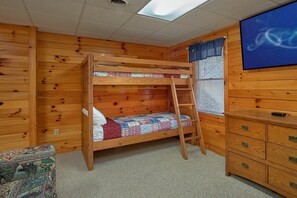 A bunk bed with a ladder, a wooden dresser with drawers, a patterned chair, and a window with blinds. - Saw'n Logs | Hot Tub, Pigeon Forge, Fireplace + Free Attraction Tickets (Pigeon Forge)