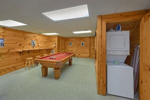 A pool table in a room with wooden walls, a refrigerator, and a door leading to another area. - Saw'n Logs | Hot Tub, Pigeon Forge, Fireplace + Free Attraction Tickets (Pigeon Forge)