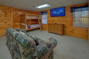 A room with a bunk bed, a dresser, a television, and a patterned sofa. - Saw'n Logs | Hot Tub, Pigeon Forge, Fireplace + Free Attraction Tickets (Pigeon Forge)