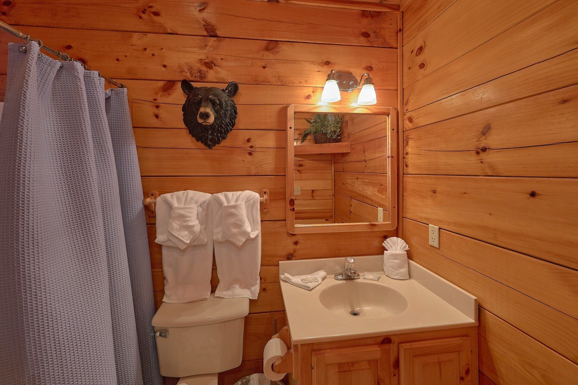 A wooden cabin bathroom with a toilet, sink, and a bear-shaped mirror.