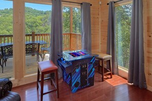 A room with a wooden deck, a table with chairs, and a gaming table. - Scenic Mountain Pool | Private Pool, Hot Tub, Near Dollywood, Game Room + Free Attraction Tickets (Pigeon Forge)