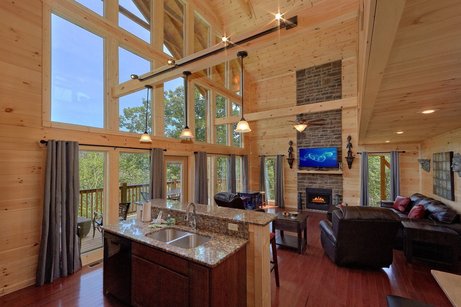 A spacious living area with a fireplace, a television mounted on the wall, and a large window overlooking a deck.
