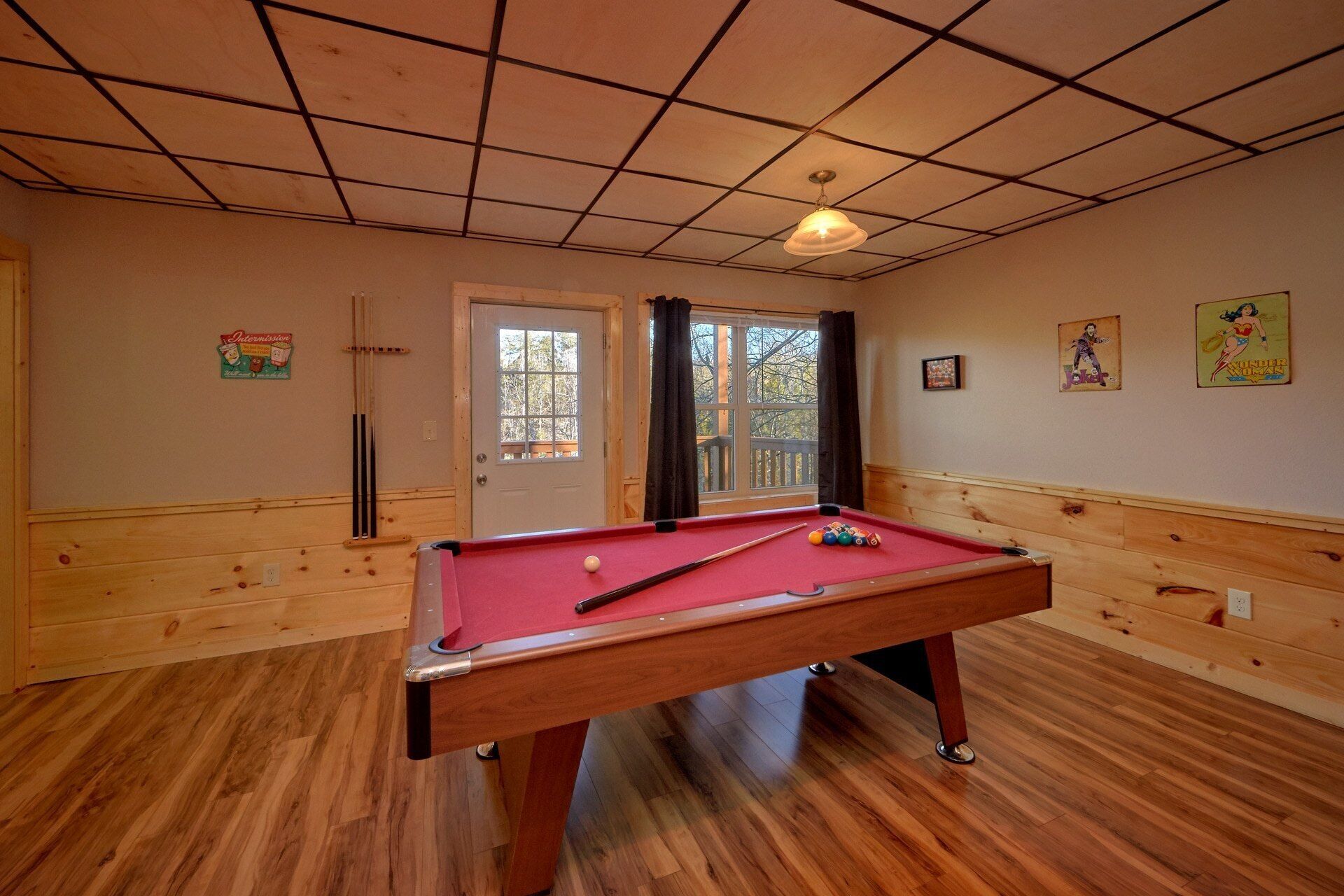 Une table de billard dans une pièce aux murs lambrés et dotée d’une fenêtre avec des rideaux.