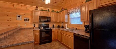 A kitchen with wooden cabinets, a black refrigerator, a microwave, a stove, and a sink.