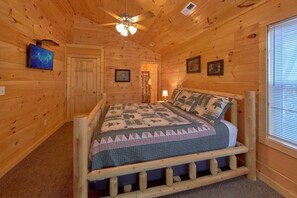Ein Zimmer einer Holzhütte mit einem Bett, einem Deckenventilator und einem Fenster mit Jalousien.
