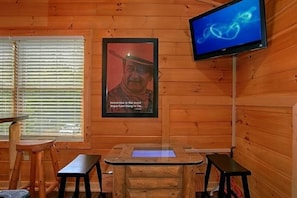 A wooden cabin interior with a wooden table, two benches, a television mounted on the wall, and a poster with a quote. - Simply Irresistible | Theater, Hot Tub, Game Room, Pigeon Forge, Fireplace + Free Attraction Tickets (Pigeon Forge)