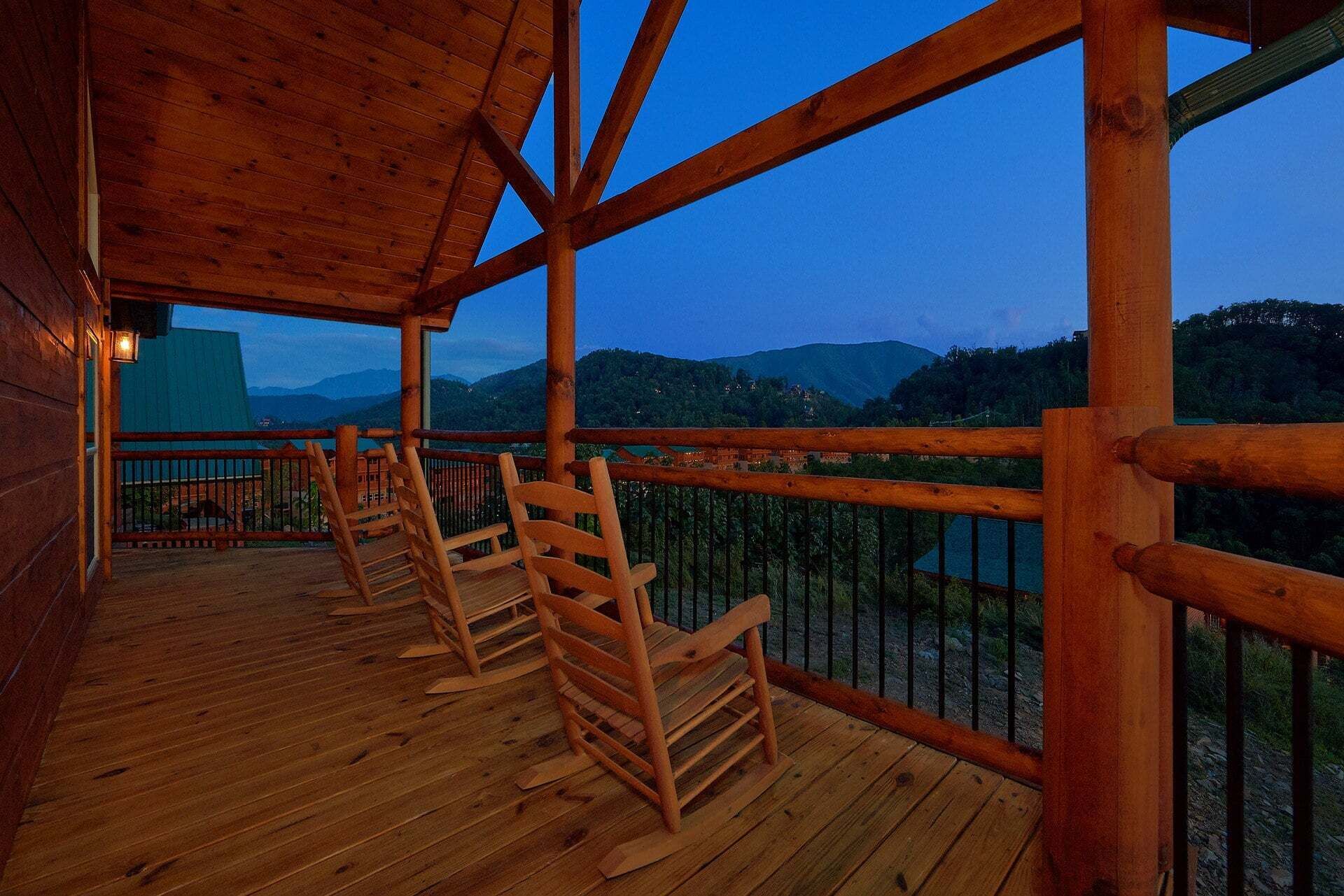 Una terraza de madera con sillas, baranda y vista a un paisaje montañoso.